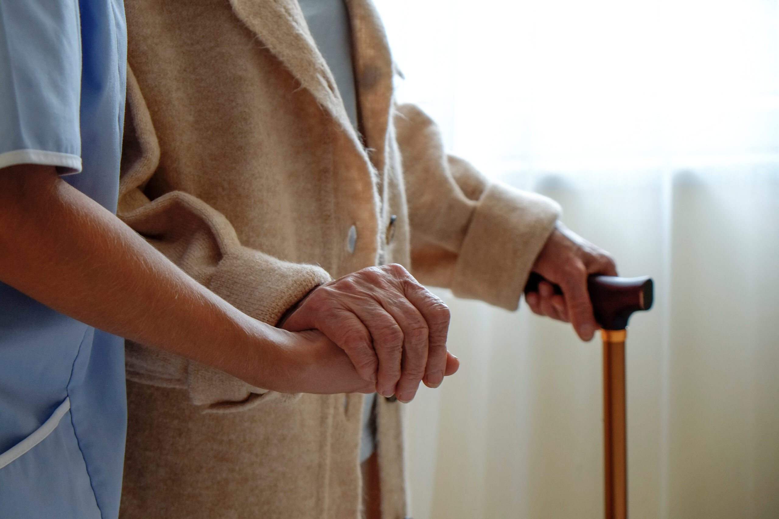Une femme âgée tenant une canne à quatre pieds dans un établissement de soins pour personnes âgées. Une infirmière hospitalière s'occupant d'une femme âgée avec une canne dans une maison de retraite. Arrière-plan, gros plan sur des mains à la peau ridée.